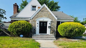 A two-story house with a stone facade, a front porch, and two well-maintained bushes.