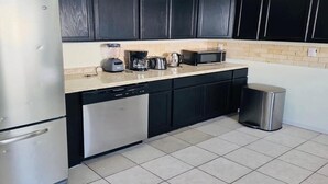 A kitchen with black cabinets, a stainless steel refrigerator, a microwave, and a coffee maker on the countertop.
