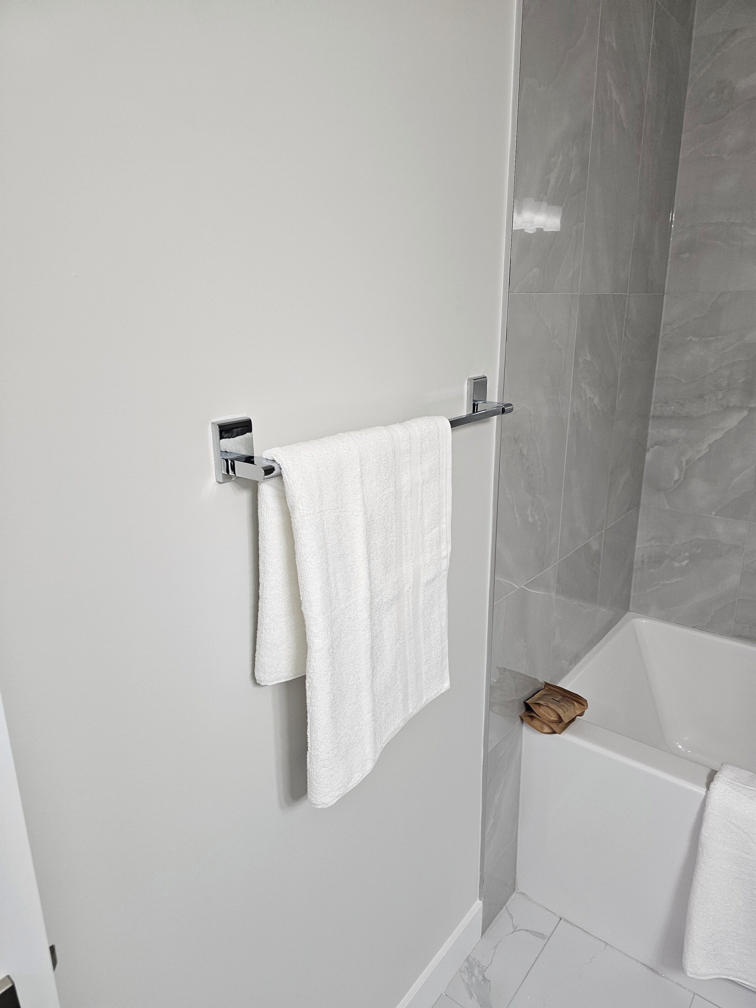 A bathroom with a white towel hanging on a metal towel rack, a glass shower enclosure, and a bathtub.