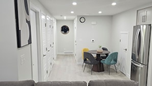 Una cocina moderna con un refrigerador de acero inoxidable, una zona de comedor con una mesa redonda y sillas, y un pasillo con puertas blancas y un espejo.
