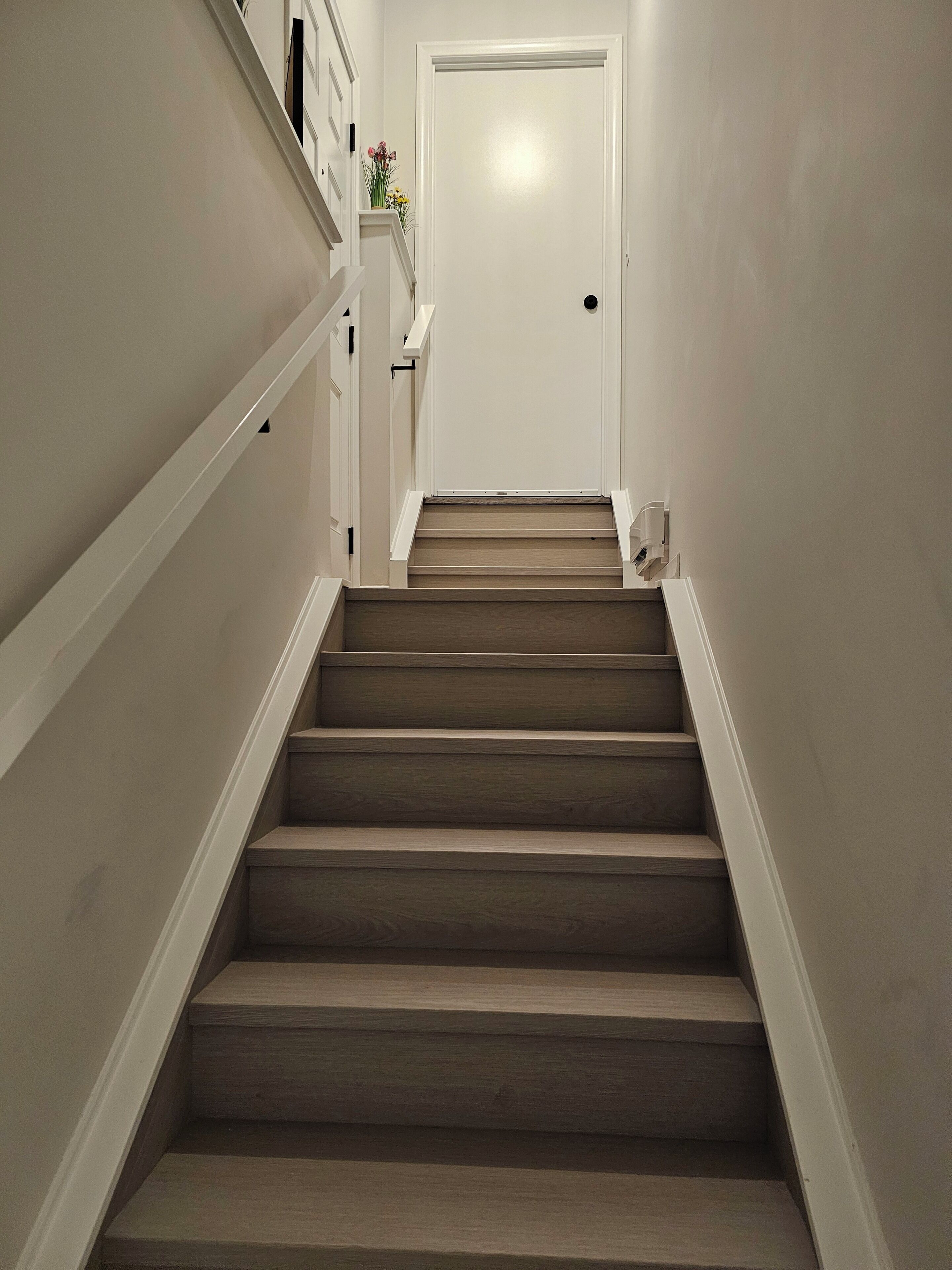 Una escalera de madera con barandillas blancas que lleva a una puerta cerrada.