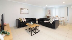 Un salon moderne avec deux canapés noirs, une table basse en bois et un coin repas comprenant une table et des chaises blanches.