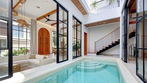 A spacious indoor pool area with a modern design, large windows, and a staircase leading to an upper level. - Villa Kala (Canggu)
