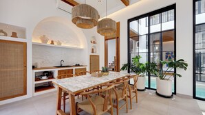 A modern kitchen with a marble countertop, wooden chairs, and large windows. - Villa Kala (Canggu)