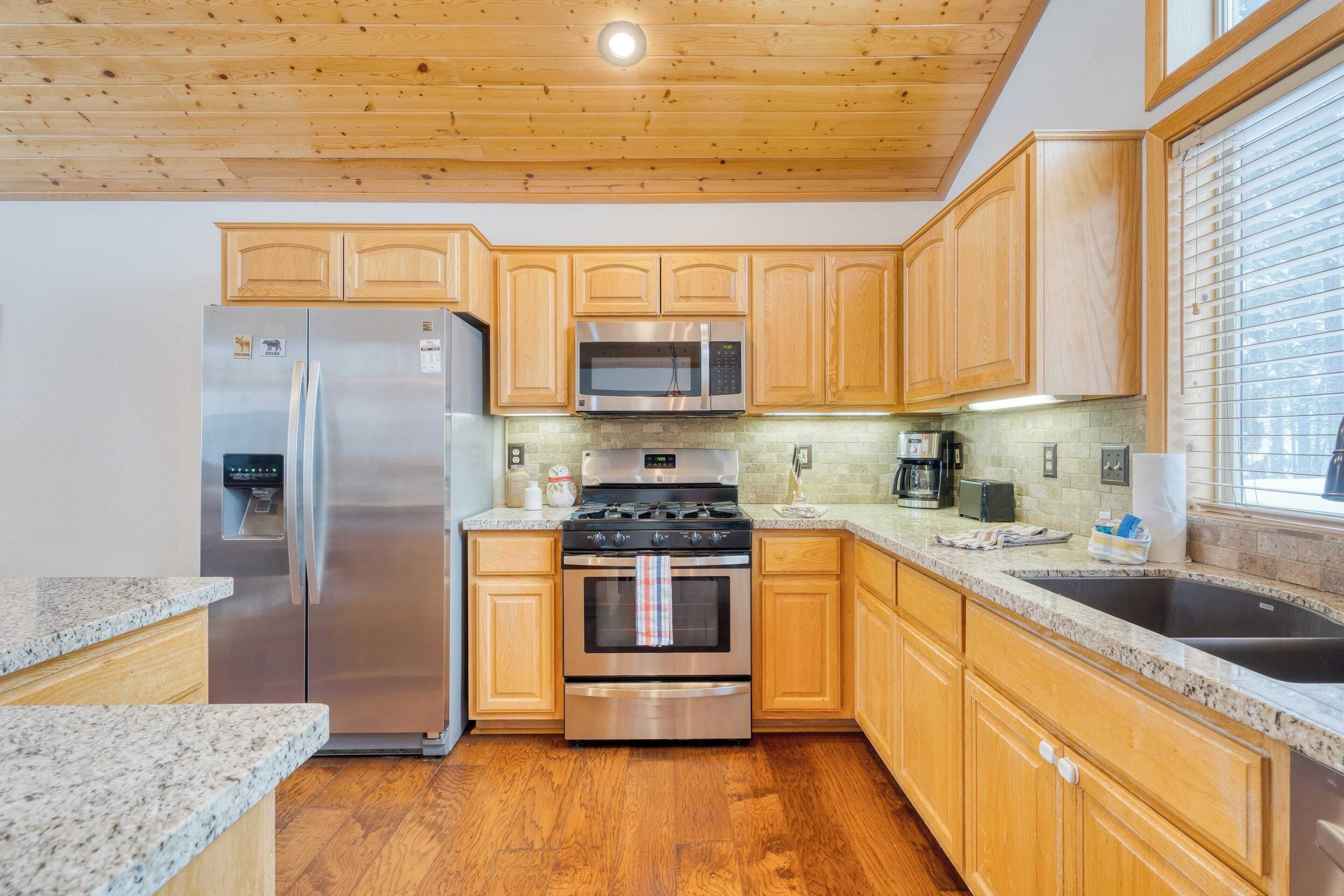 A kitchen with wooden cabinets, stainless steel appliances, granite countertops, and a wooden floor.