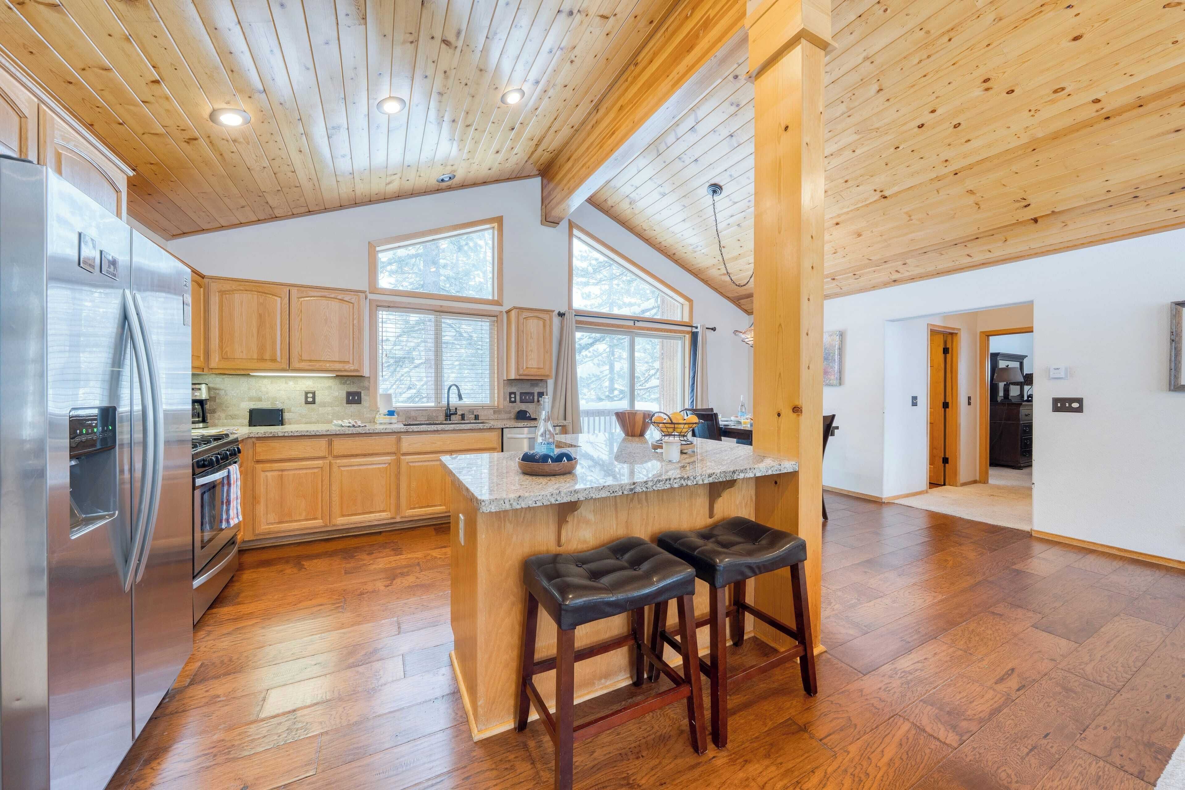 A spacious kitchen with wooden cabinets, a stainless steel refrigerator, and a large island with stools.