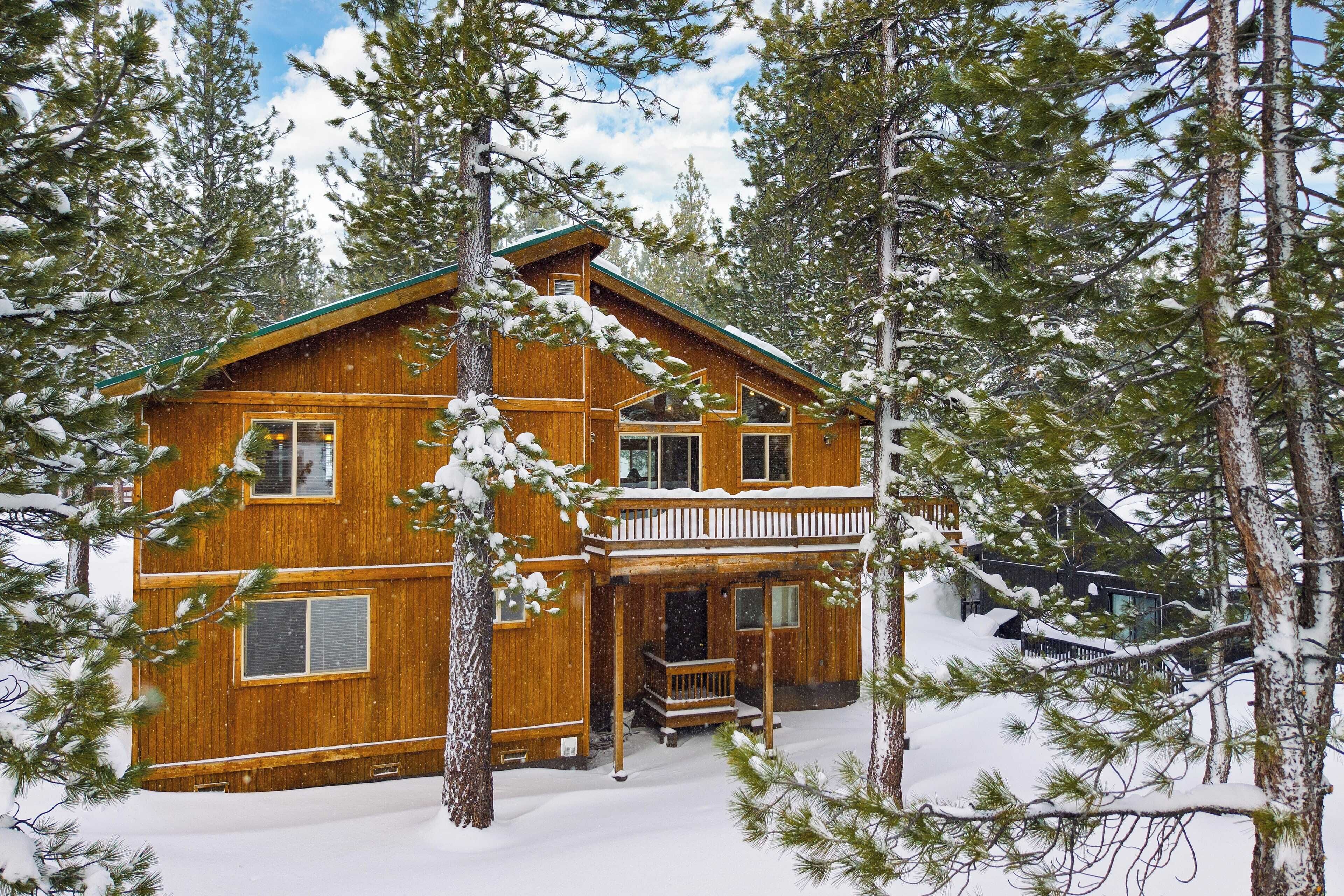 A wooden cabin with a balcony, surrounded by snow-covered trees.