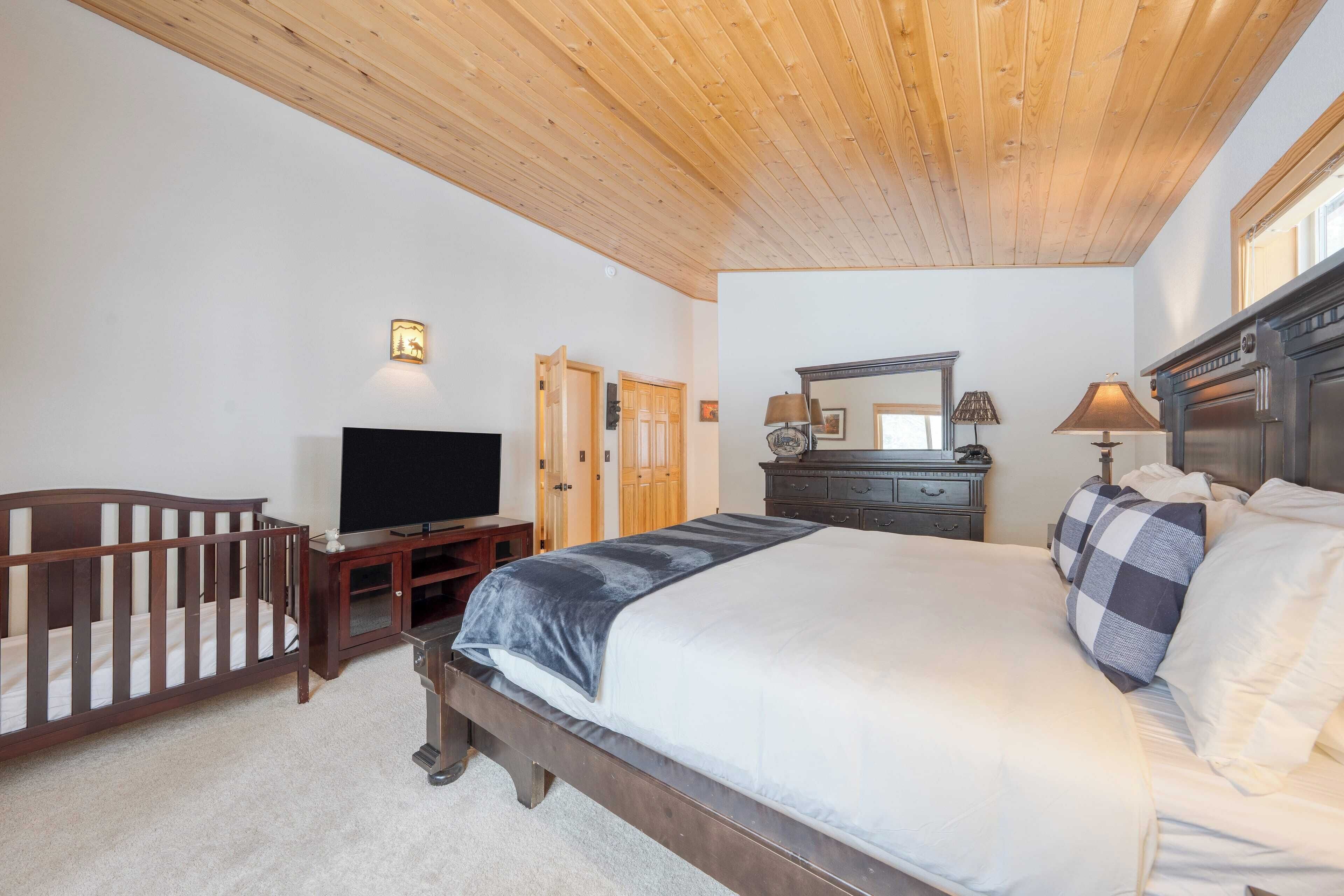 A bedroom with a wooden ceiling, a bed with a checkered blanket, a television, a dresser, and a mirror.