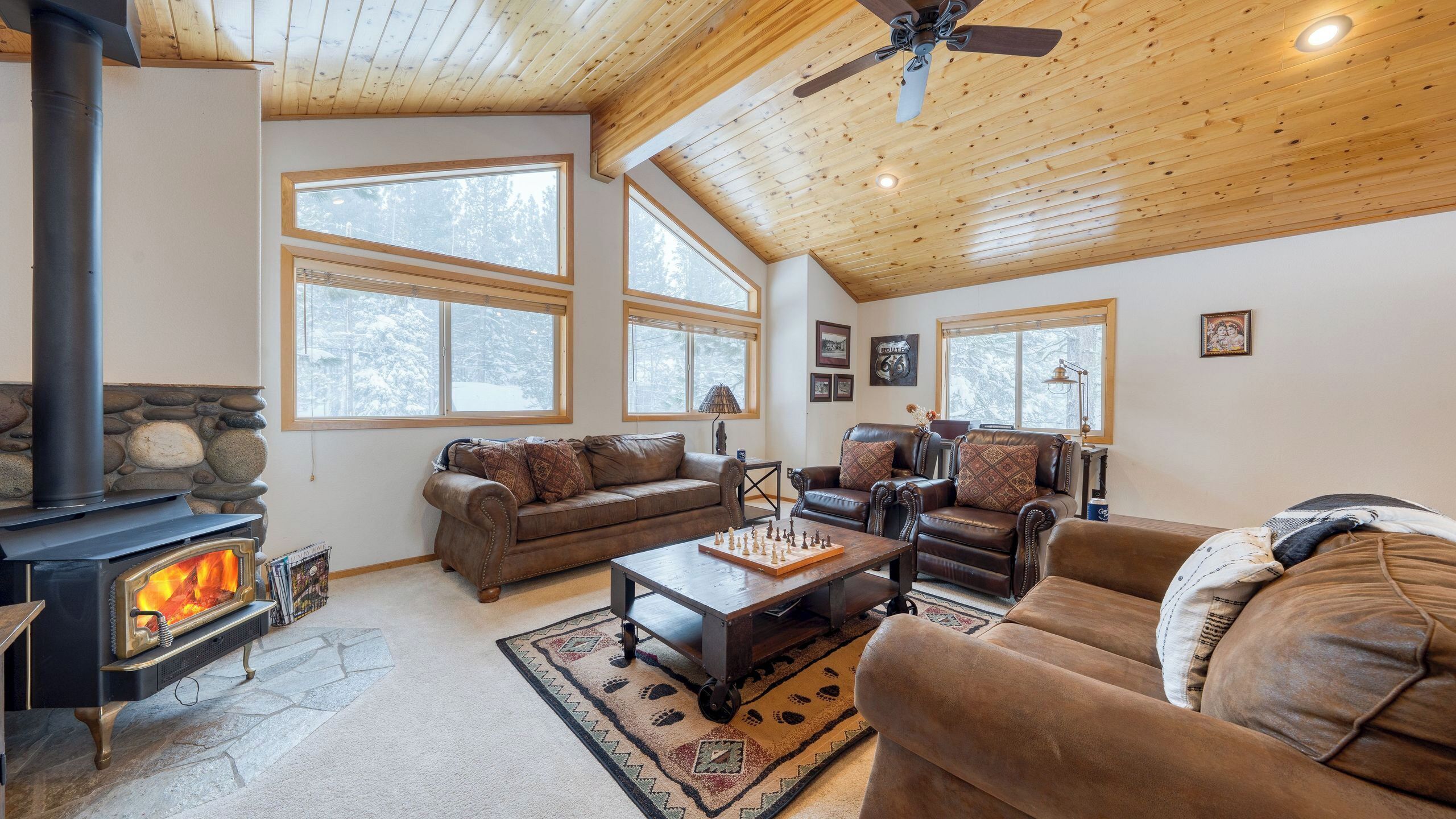 A cozy living room with a fireplace, leather sofas, a coffee table, and large windows.