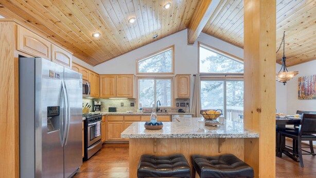 A spacious kitchen with wooden cabinets, a stainless steel refrigerator, a granite countertop, and a large island with two stools. - Oslo Haus by Avantstay Cabin Retreat Near Northstar + Downtown Truckee (Truckee)
