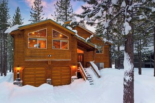 Uma cabana de madeira com garagem, escadas e paisagem coberta de neve.