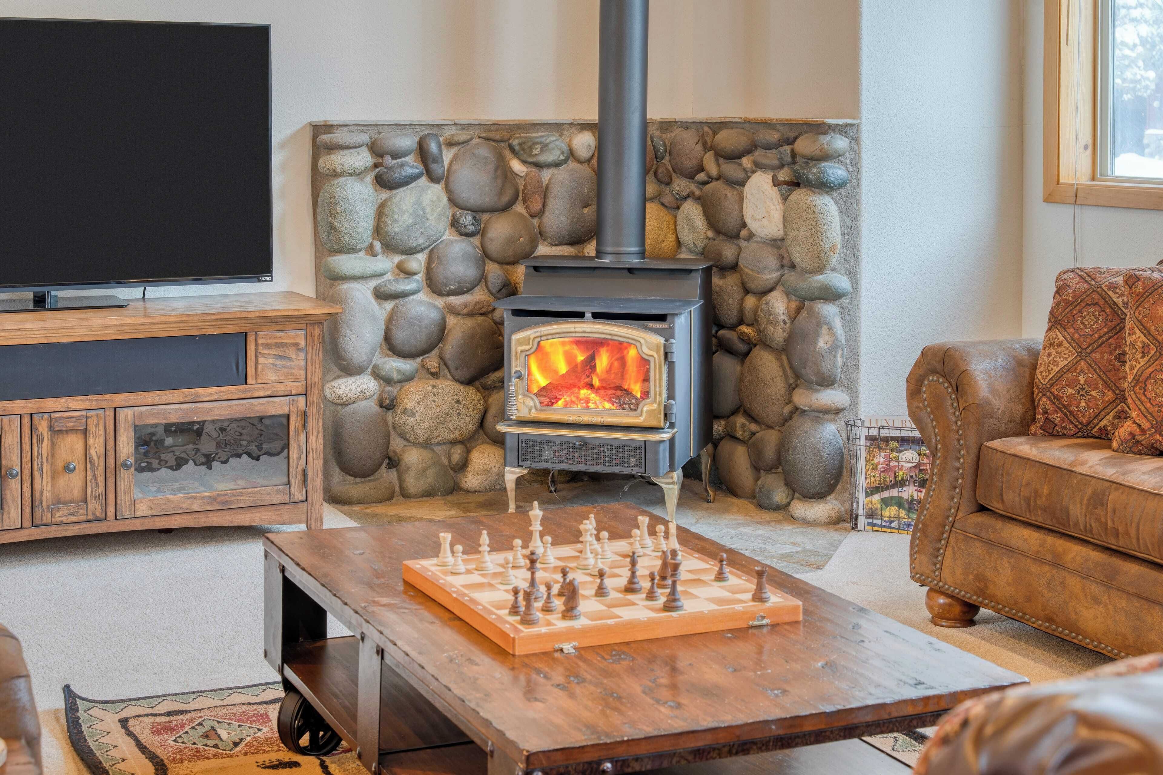 Un salon chaleureux avec une cheminée en pierre, un téléviseur à écran plat, une table basse en bois sur laquelle sont posés des pièces d’échecs, et un canapé en cuir.