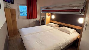 A bunk bed with a wooden headboard, a bedside table with a lamp, and a window with curtains. - B&B HOTEL Lisieux Parc des Expositions (Lisieux)