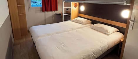 Una cama litera con cabecera de madera, una mesita de noche con lámpara y una ventana con cortinas.