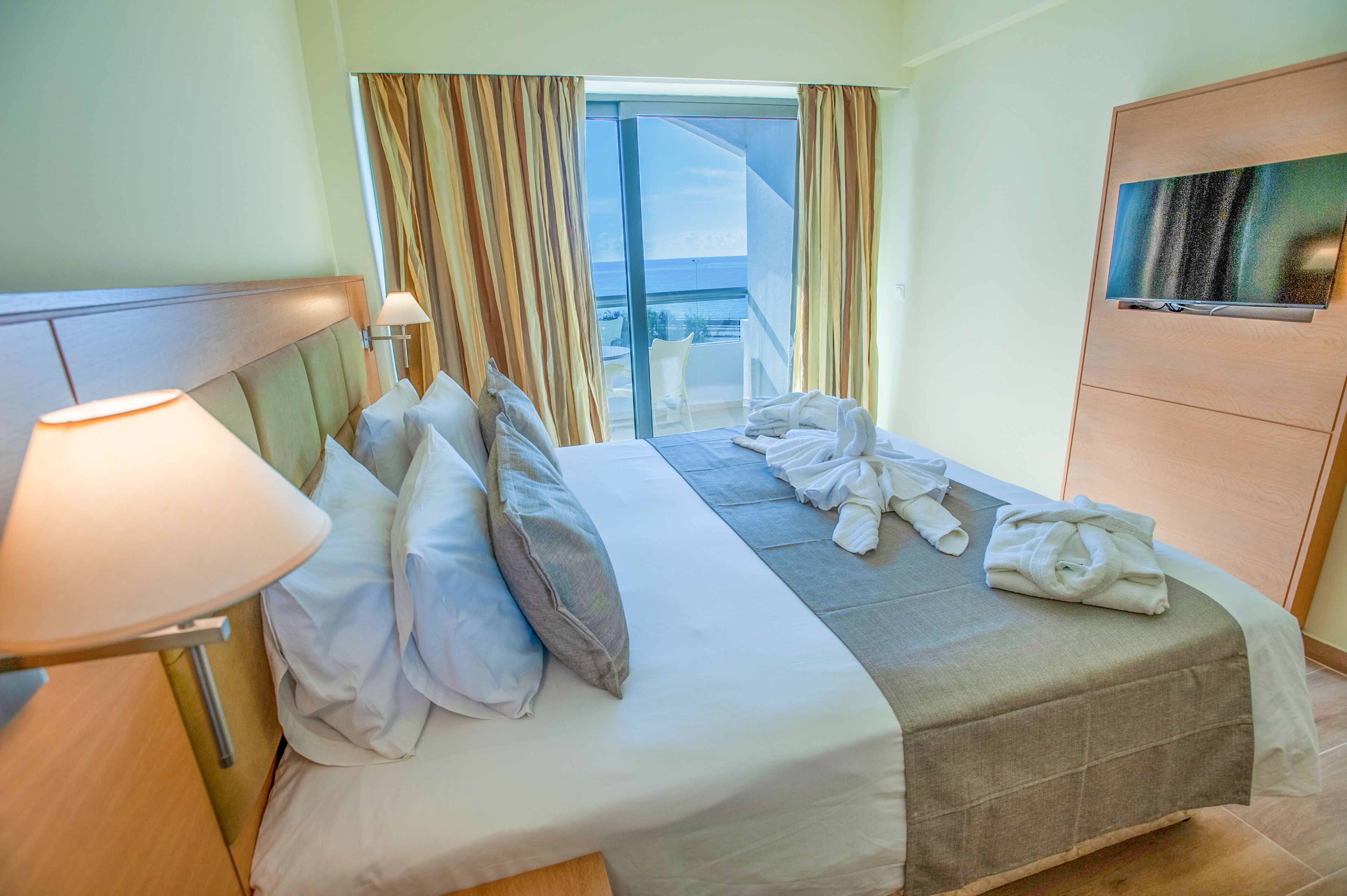 A hotel room with a bed, a TV, a lamp, and a view of the outside.