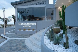 The exterior of Rhodos Horizon Marina with a sign, a modern design, and a landscaped area with cacti and white pebbles.
