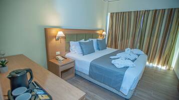 A hotel room with a bed, bedside lamps, a nightstand, a wooden desk, and a window with curtains.