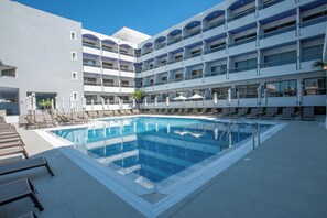 A hotel with a swimming pool, multiple balconies, and sun loungers.