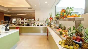 A buffet with a variety of fruits and vegetables, including pineapples, oranges, and apples, arranged on a counter.