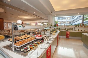 A buffet area with various food items and a view of a modern building in the background. - Rhodos Horizon Marina (Rhodes)