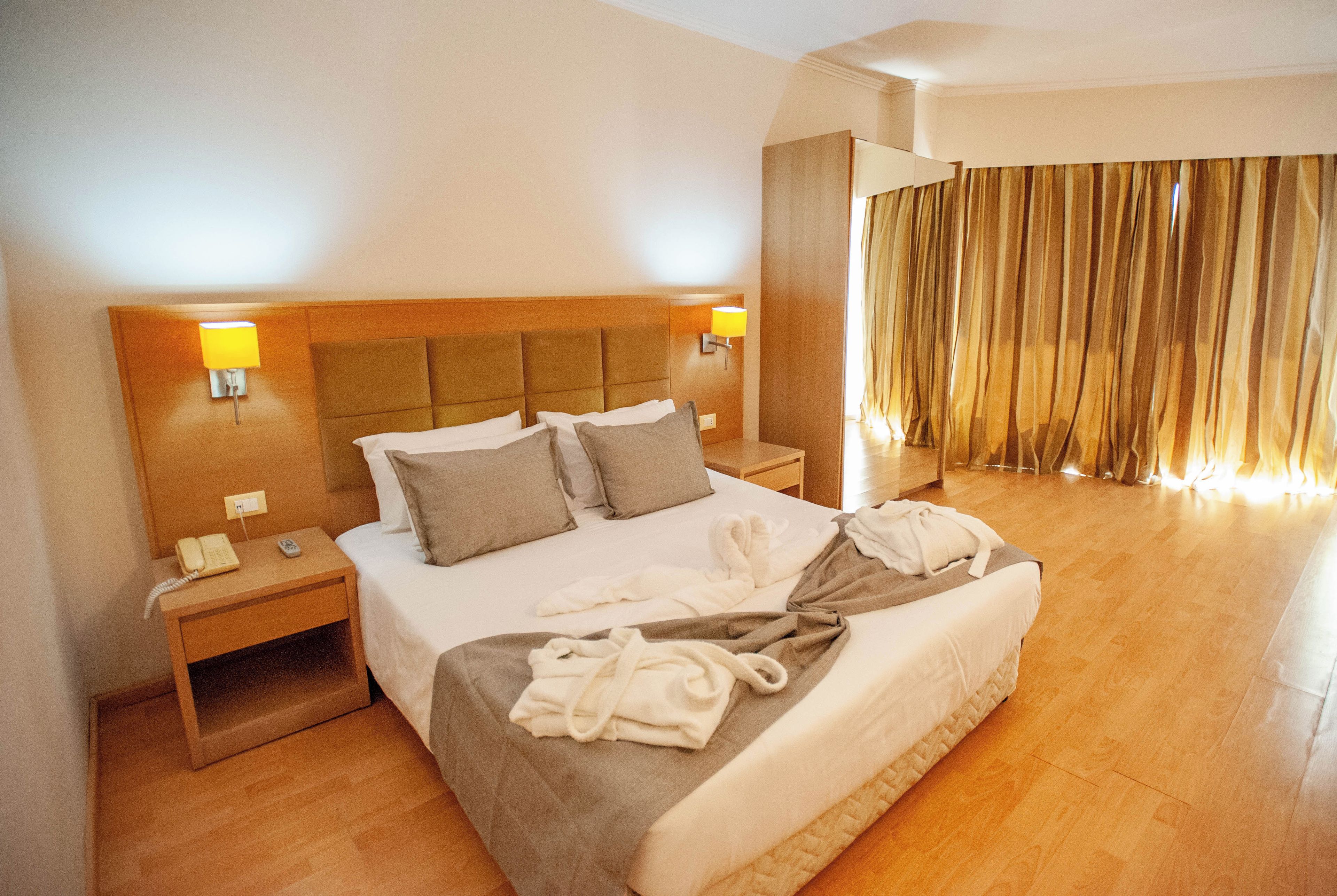 A hotel room with a large bed, two bedside tables, a telephone, and a window with curtains.