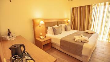 Een hotelkamer met een bed, bedlampjes, een nachtkastje met een telefoon, een tafel met een koffiezetapparaat en een raam met gordijnen.