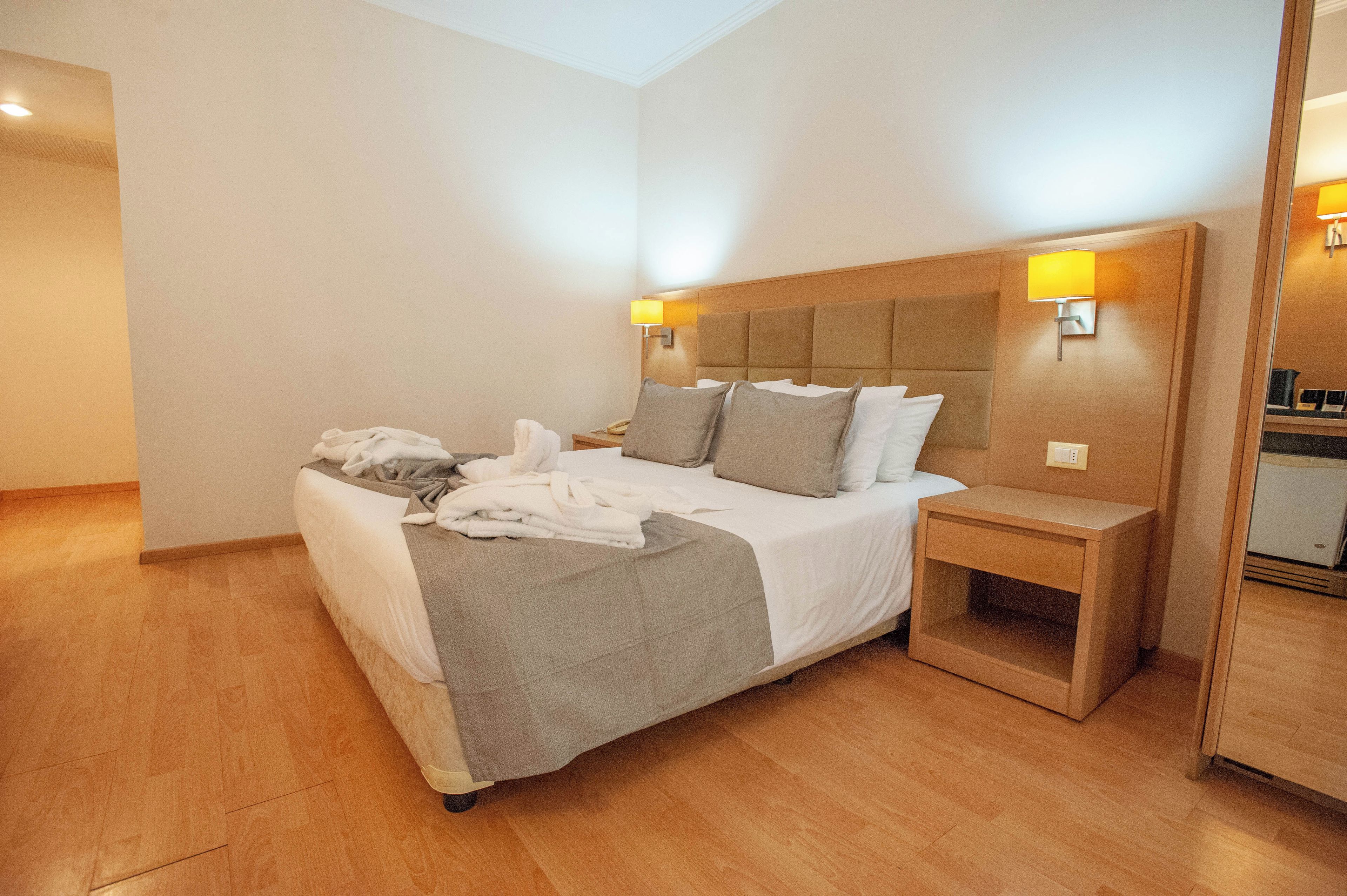 A hotel room with a bed, bedside tables, and a mirror.