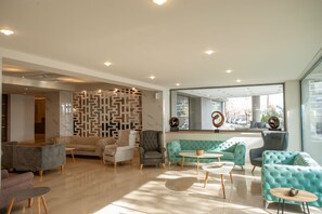 A modern lobby with a geometric wall design, plush seating, and a large window offering a city view.