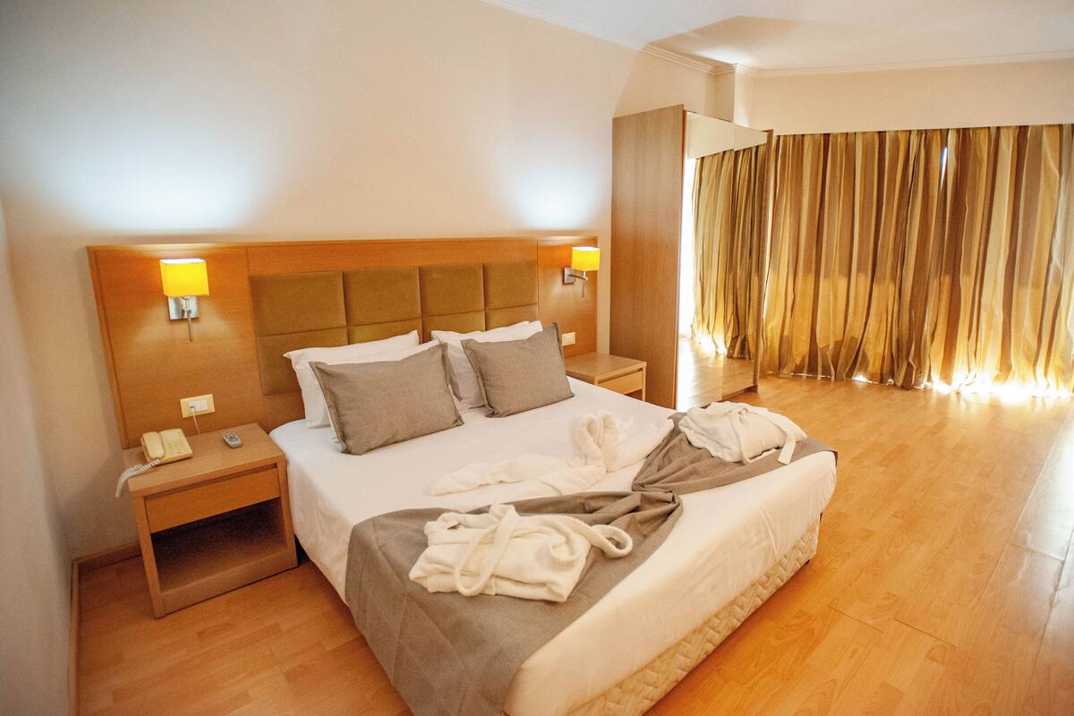 A hotel room with a large bed, two bedside tables, a telephone, and a window with curtains.