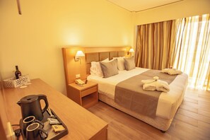 A hotel room with a bed, bedside lamps, a nightstand with a phone, a table with a coffee maker, and a window with curtains. - Rhodos Horizon Marina (Rhodes)