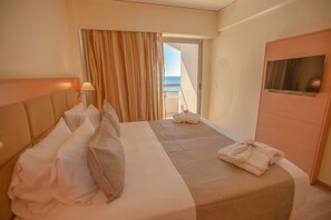 A hotel room with a bed, a TV, a balcony with curtains, and a view of the sea.