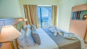A hotel room with a bed, a TV, a lamp, and a view of the outside. - Rhodos Horizon Marina (Rhodes)