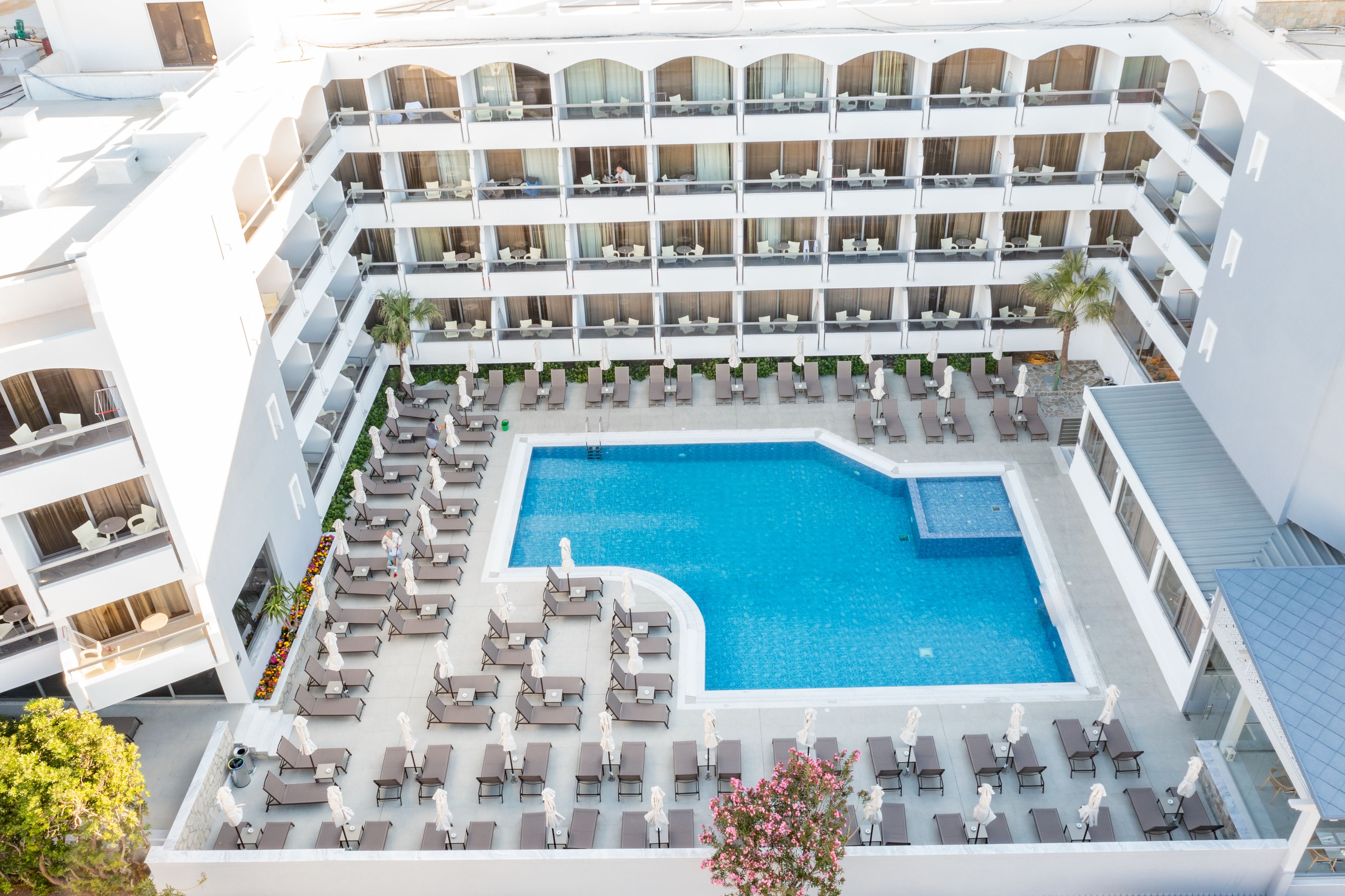 Ett hotell med flera våningar, en central pool omgiven av solstolar och en liten trädgårdsdel.