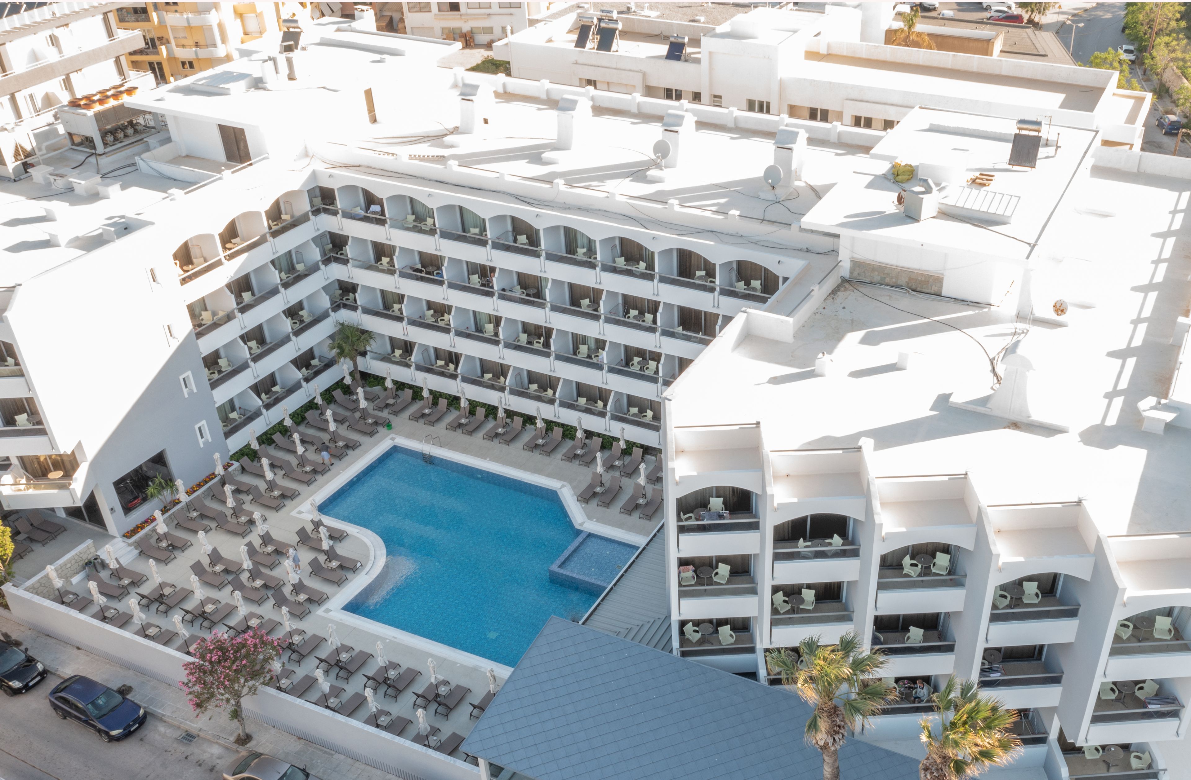 Ett hotell med flera balkonger, en central pool och en takterrass.