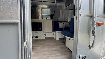A van interior with a kitchenette, seating area, and a door with a doormat that reads "Adventure Inspired by Airstream."
