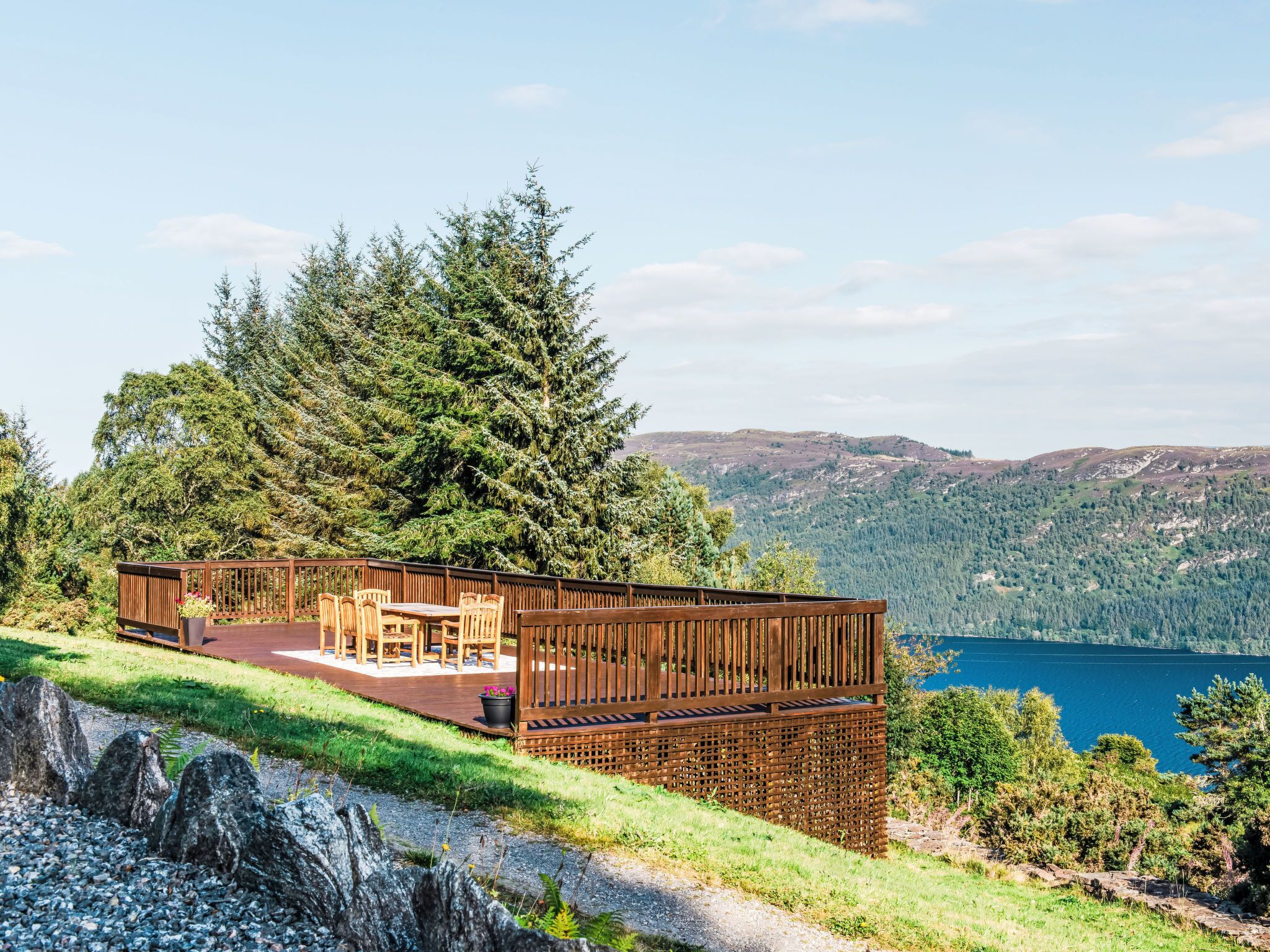 A wooden deck with outdoor furniture overlooking a lake and forested hills.
