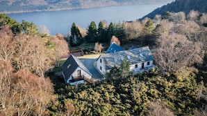 A house with a sloped roof, surrounded by dense forest and a lake. - Drover's Lodge by Interhome (Drumnadrochit)