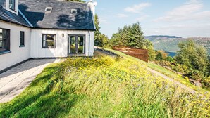 A white house with a dark roof, large windows, and a deck overlooking a valley. - Drover's Lodge by Interhome (Drumnadrochit)