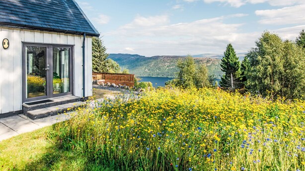 A modern house with a large glass door, a deck, and a view of a lake and mountains. - Drover's Lodge by Interhome (Drumnadrochit)
