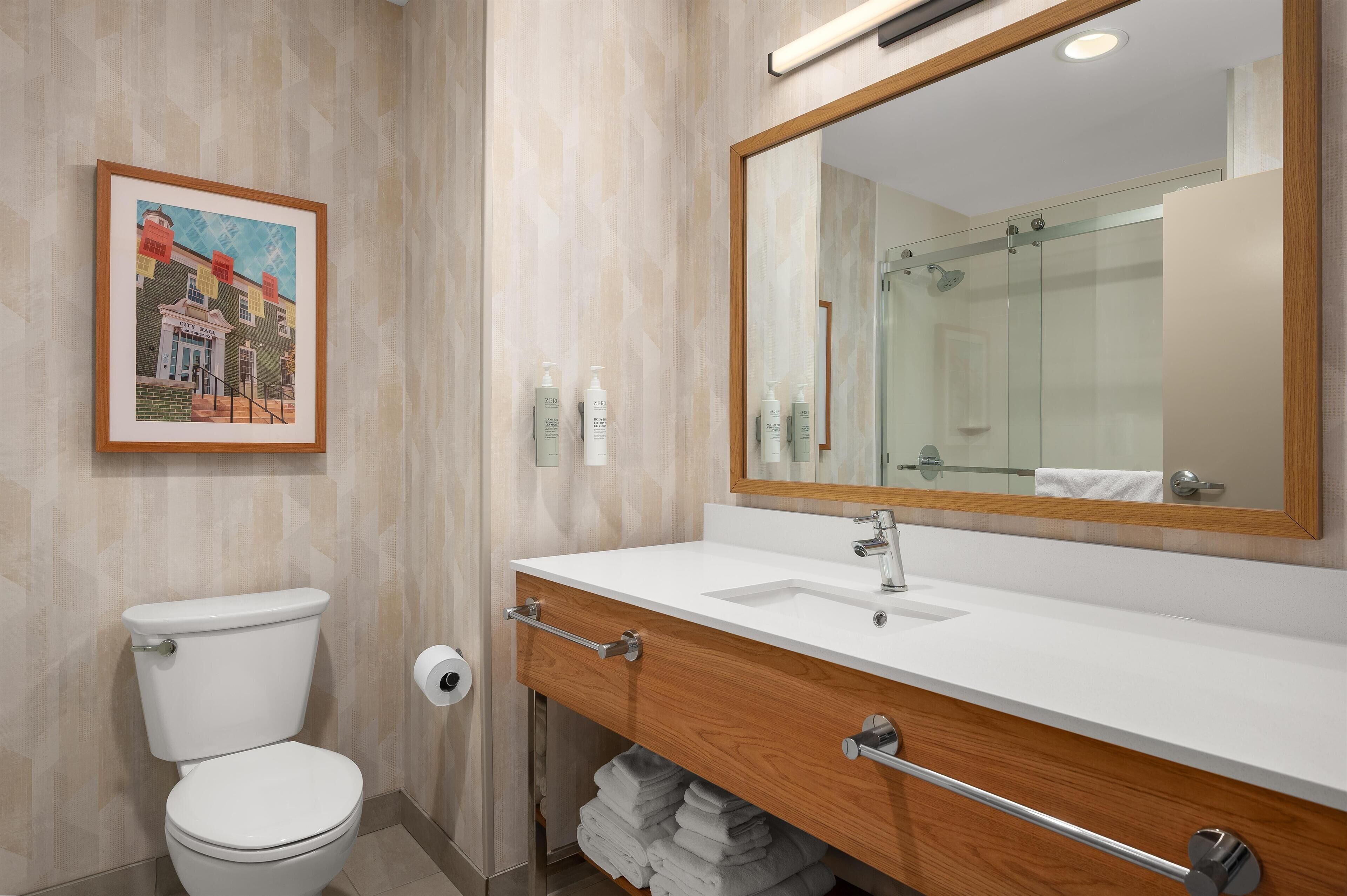 A modern bathroom with a toilet, sink, vanity, and a large mirror.