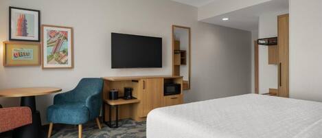 A hotel room with a bed, a desk with a chair, a television, and a small cabinet.