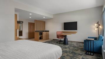 A hotel room with a large bed, a desk with a chair, a TV, and a seating area with a sofa.