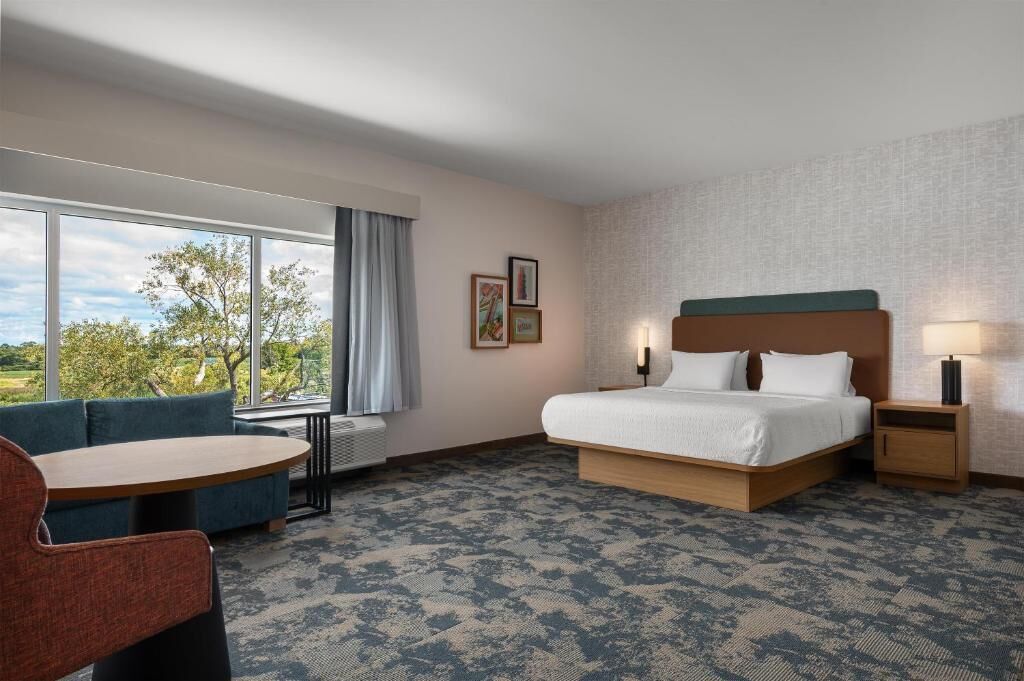 Habitación de hotel con una cama grande, un sofá, una mesita y una ventana que da a árboles.