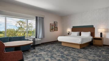 Habitación de hotel con una cama grande, un sofá, una mesita y una ventana que da a árboles.