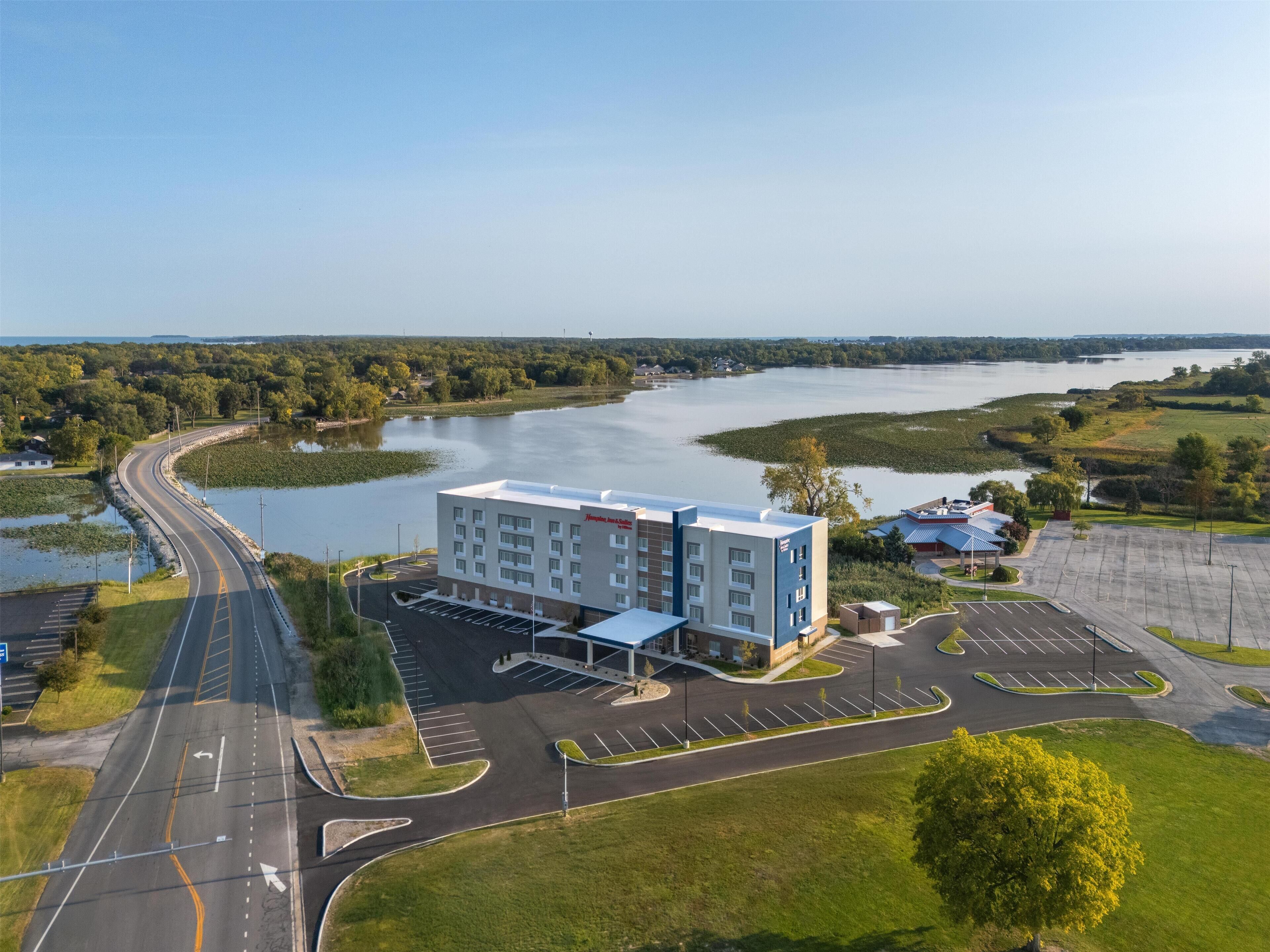 A hotel with a parking lot, a road curving around a body of water, and a building with a flat roof.