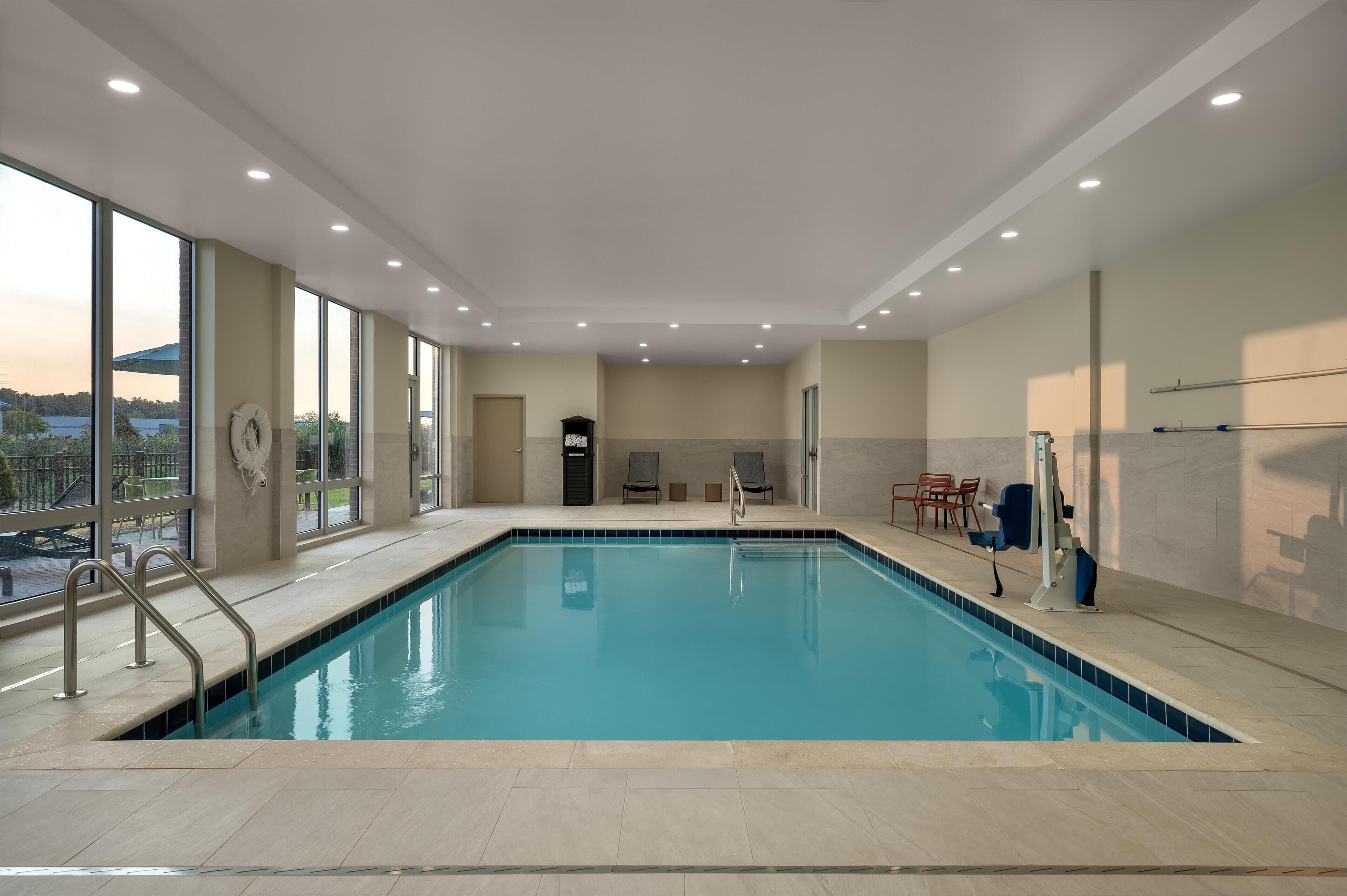 A modern indoor swimming pool with clear glass walls, a tiled floor, and a view of the outdoors.