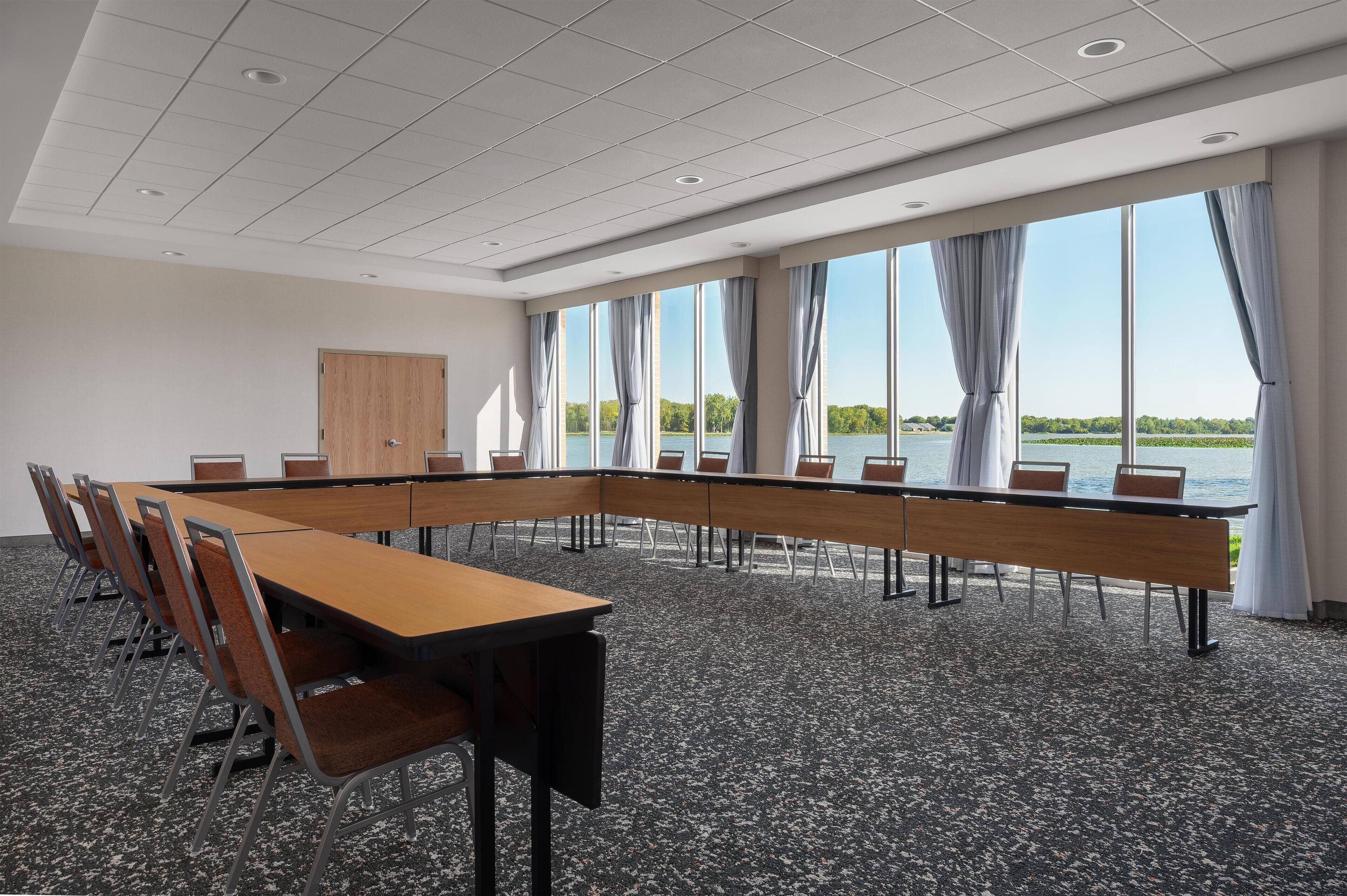 Un salón de conferencias con una larga mesa, sillas y grandes ventanales con vistas al agua.