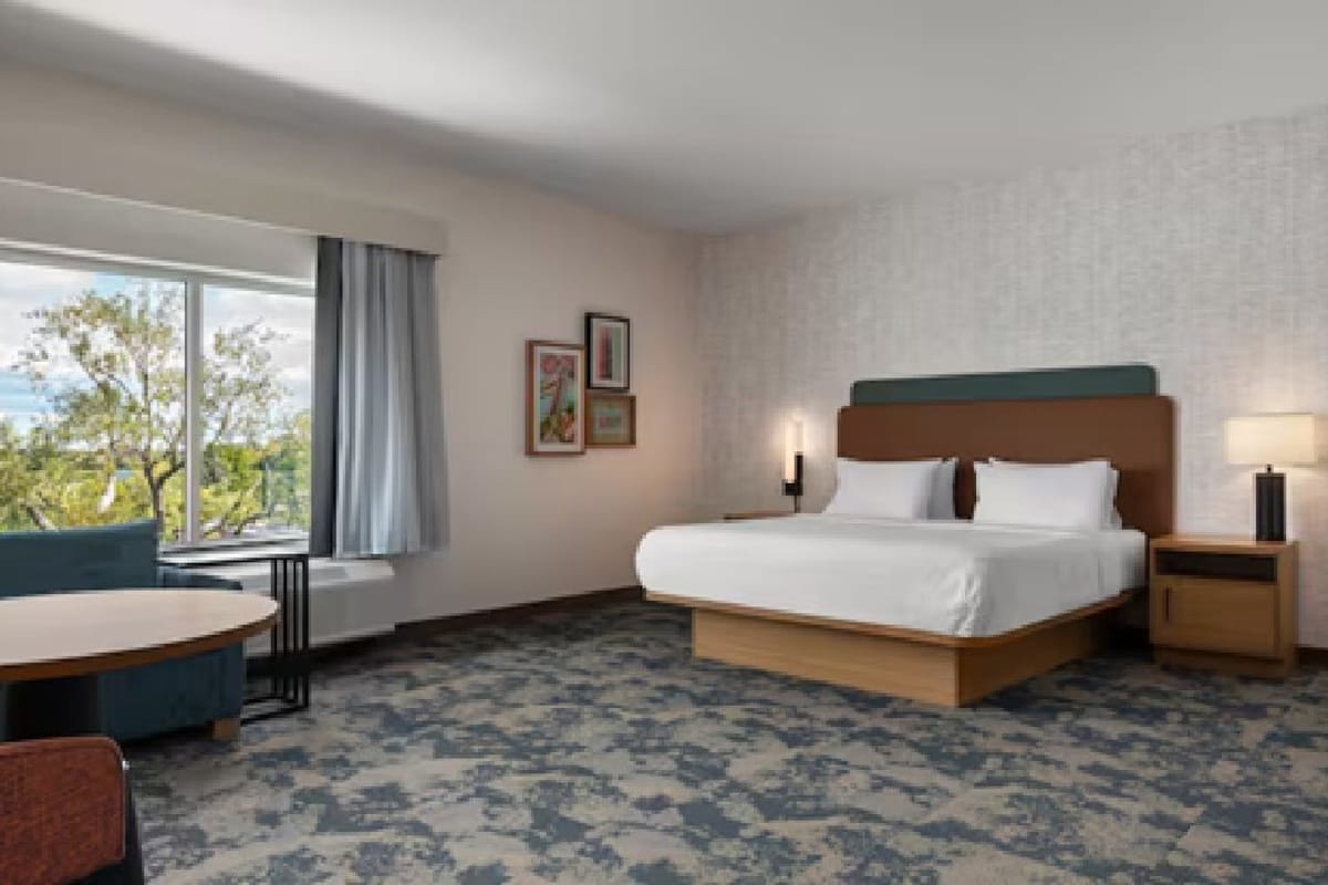 Ein Hotelzimmer mit einem großen Bett, einer Sitzecke mit einem Tisch und Blick auf Bäume.