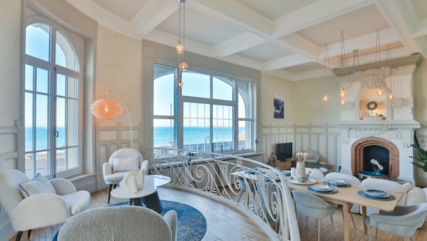 Een ruime kamer met balkon en uitzicht op zee, voorzien van een open haard en een eethoek.