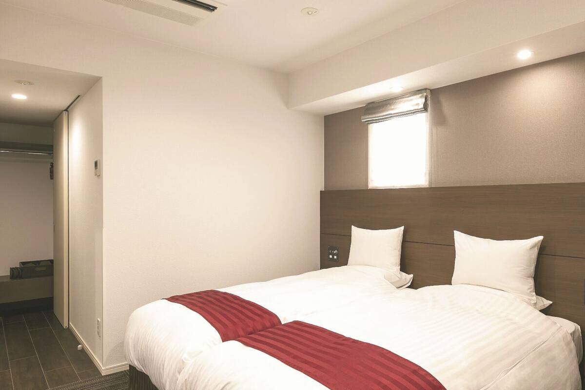 A hotel room with a large bed, a wooden headboard, a small window, and a door leading to a bathroom.